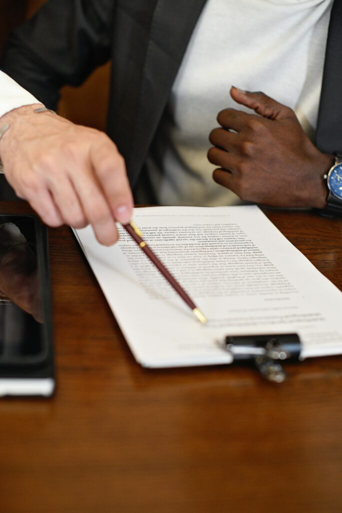 Two adults reviewing and discussing a business contract with a pen and clipboard on a wooden table.